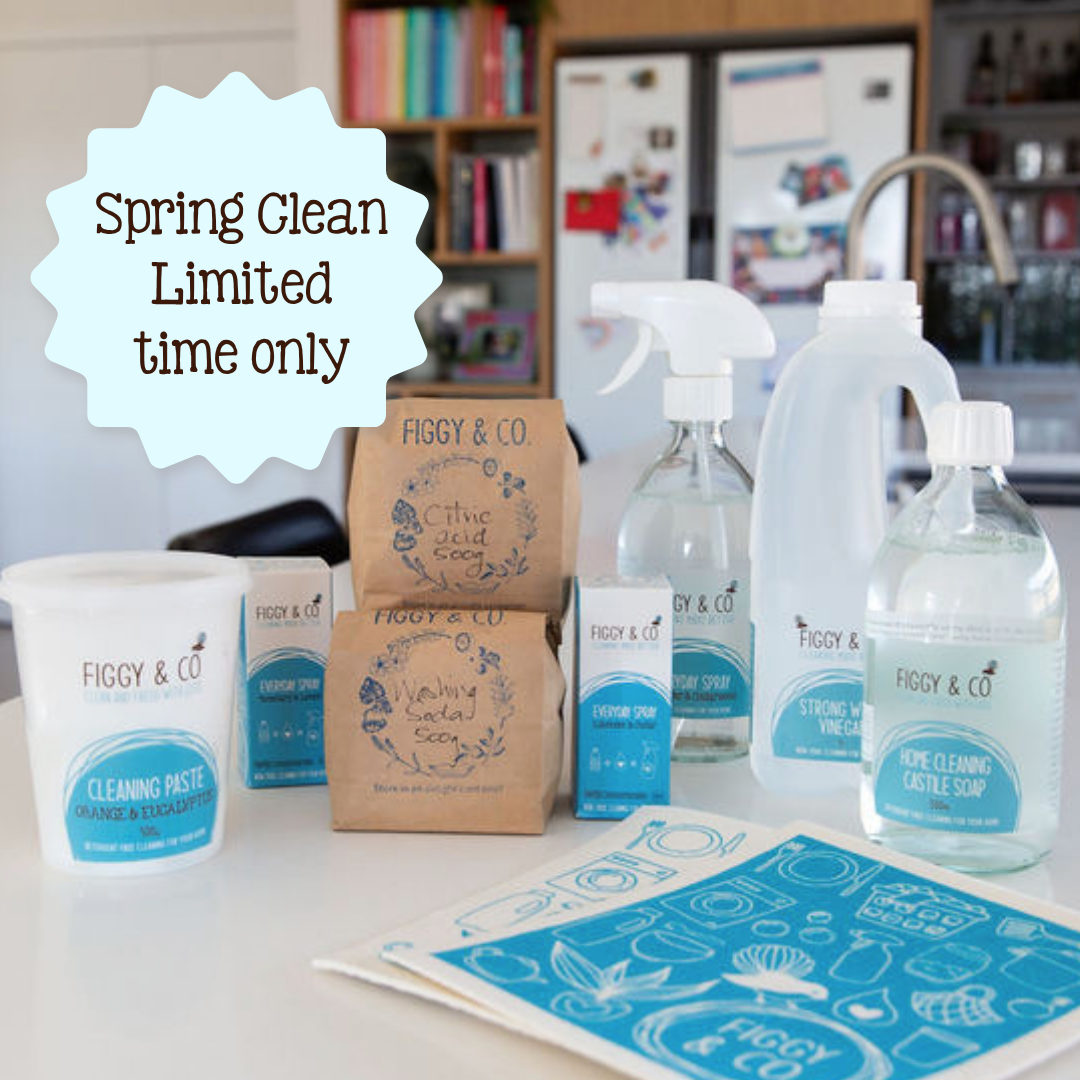 A spring cleaning product set from Figgy &amp; Co arranged on a kitchen counter, including castile soap, surface spray, oxygen bleach, citric acid, cleaning paste, washing soda, vinegar, and cleaning sponge, alongside paper bags and a blue cleaning guide sheet. A light blue starburst overlay reads 'Spring Clean Limited time only'.