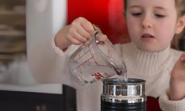 Child pouring water into Nespresso milk frother cleaning it 